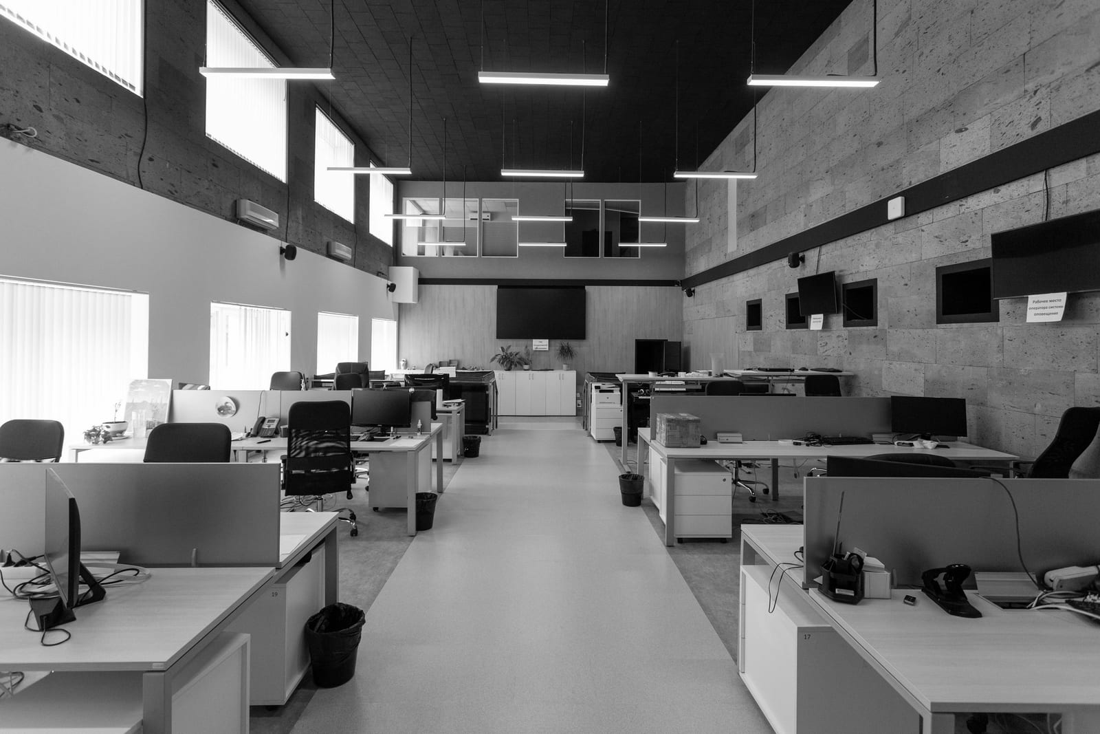 An empty open-plan office with rows of desks and monitors under linear ceiling lights